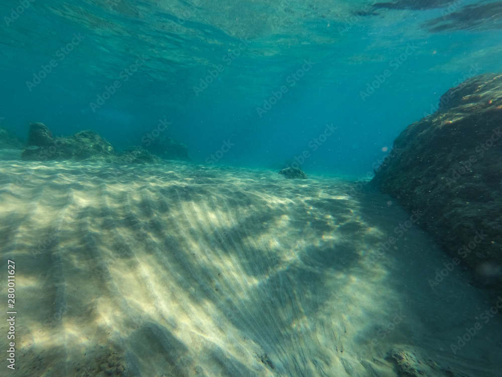 Fototapeta premium Underwater view of the rocks, sand and stones. The sandy and rocky bottom of the sea with some sun rays.
