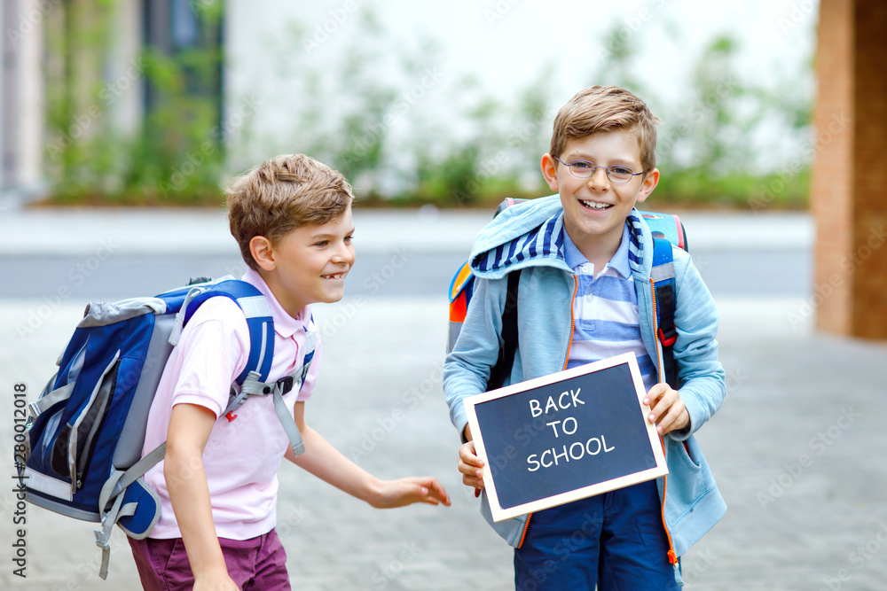 Two little kid boys with backpack or satchel. Schoolkids on the way to school. Healthy children, brothers and best friends outdoors on street leaving home. School's out on chalk desk. Happy siblings.