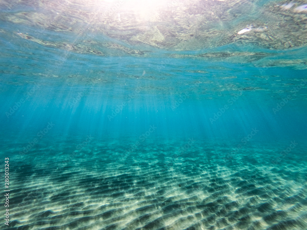 Underwater view of the rocks, sand and stones. The sandy and rocky bottom of the sea with some sun rays.