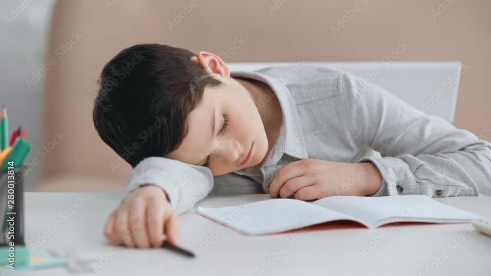 tired preteen schoolboy with pen sleeping on desk near copy book, calculator and pencils tired preteen schoolboy with pen sleeping on desk near copy book, calculator and pencils