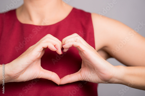Closeup hands of a beautiful woman in stylish red outfit making heart shape gesture on her chest. Positive human emotion expression, Love, Caring, Body language, Health, Charity, Donation concept.