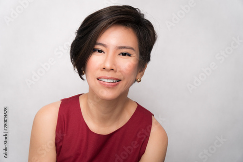 Obraz na plátně Studio portrait of a beautiful middle aged asian woman (40-50) in stylish red outfit smiling charming and cheerful on white background