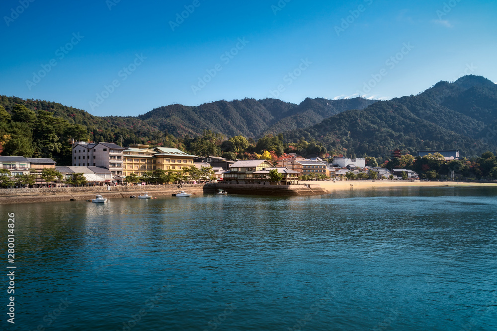 Boats near a pier at Miyajima Island in autumn with Itsukushima Shrine and Mount Misen in the background - Hiroshima Bay, Japan.