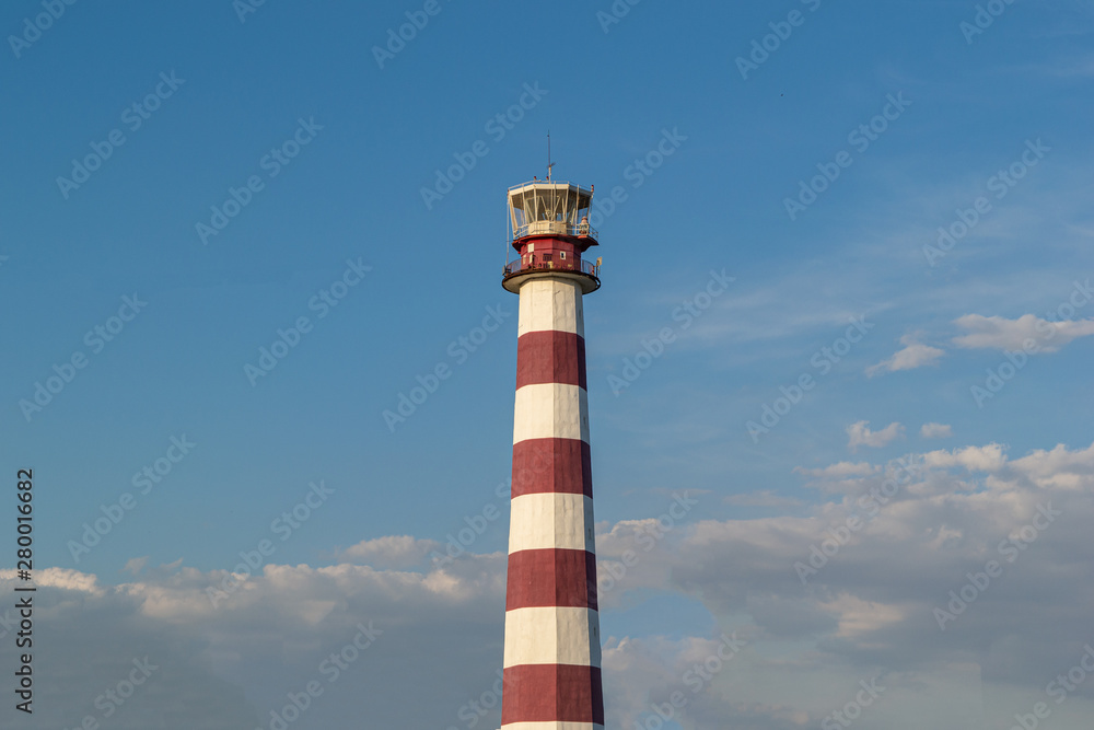 Lighthouse on the beach on a Sunny day against the blue sky.  Trees grow near the lighthouse.