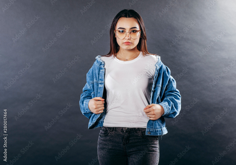 Girl wearing t-shirt with place for logo, glasses and cotton jacket posing in studio on black white background