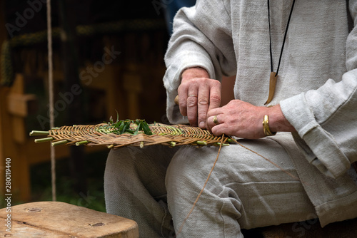 Close up of craftsman wearing rural clothes making wicker basket of twigs. Traditional handmade weaving technique at rural village