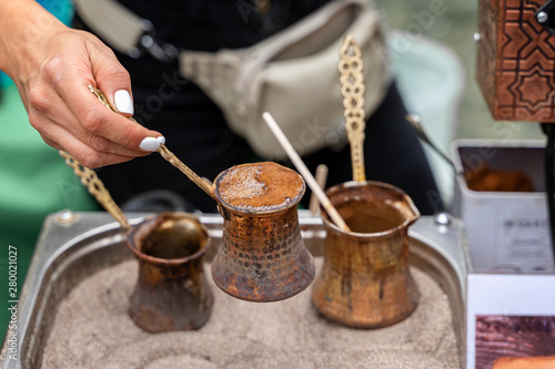 Hands of girl making traditional turkish coffee with foam in copper turk on hot sand. Coffee preparation concept