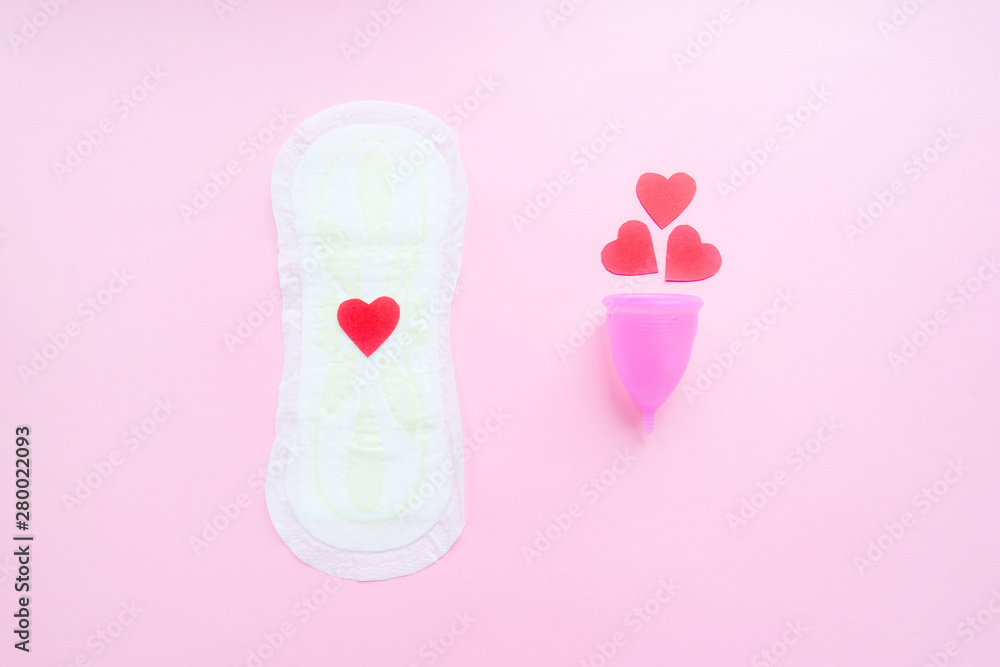 Reusable menstrual cup with red hearts and menstrual pad on pink background, Concept female intimate hygiene period products and zero waste. Flat lay, minimalism, top view. copyspace