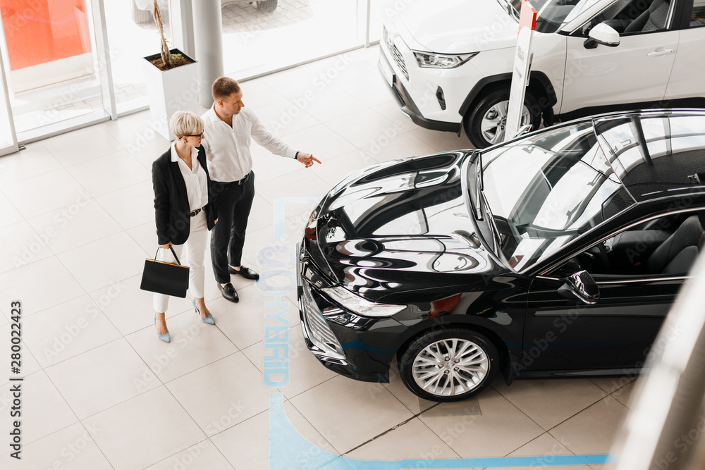 Φωτογραφία Family couple in dealership choose a car, man pointing to automobile