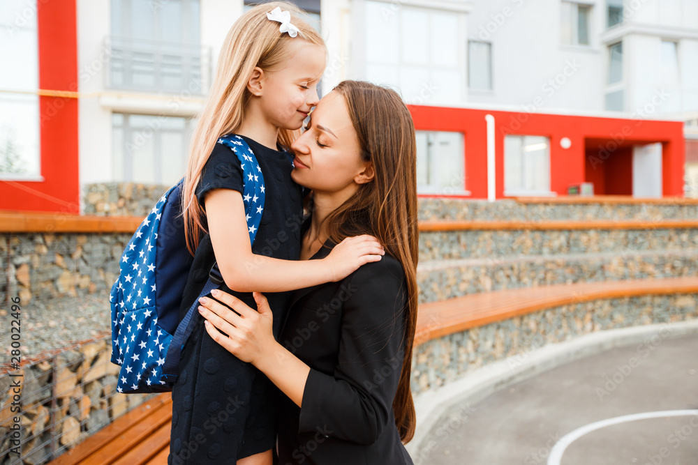 Mom leads her daughter to school. Return to school. Woman and girl with backpack behind the back. Beginning of lessons. First day of fall. Mom leads her daughter to school. Return to school. Woman and girl with backpack behind the back. Beginning of lessons. First day of fall.