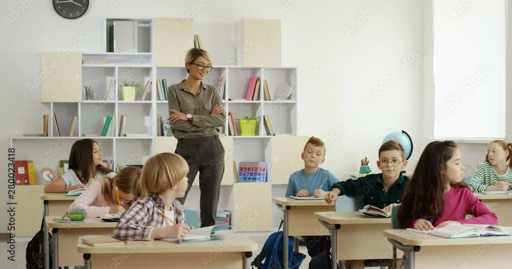 Portrait shot of the young Caucasian pretty female teacher and teen pupils at the desks smiling all together to the camera in he classroom. Portrait shot of the young Caucasian pretty female teacher and teen pupils at the desks smiling all together to the camera in he classroom.