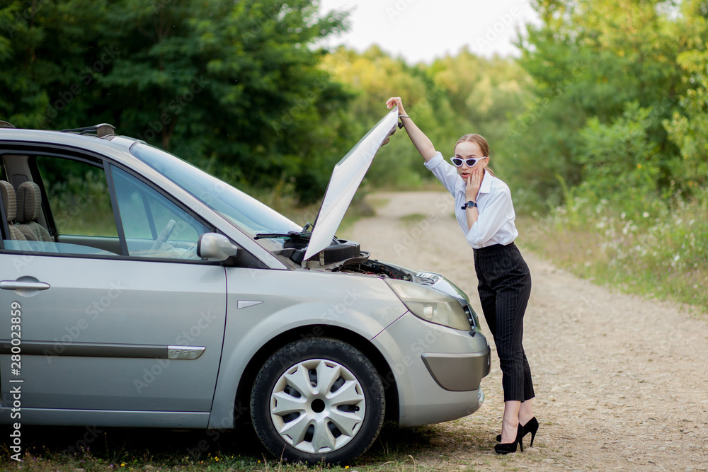 Young woman by the roadside after her car has broken down She opened the hood to see the damage Young woman by the roadside after her car has broken down She opened the hood to see the damage