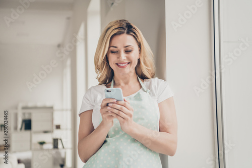 Portrait of her she nice-looking charming cute attractive lovely cheerful cheery wavy-haired girl holding in hands cell rest relax wi-fi web in light white interior kitchen studio