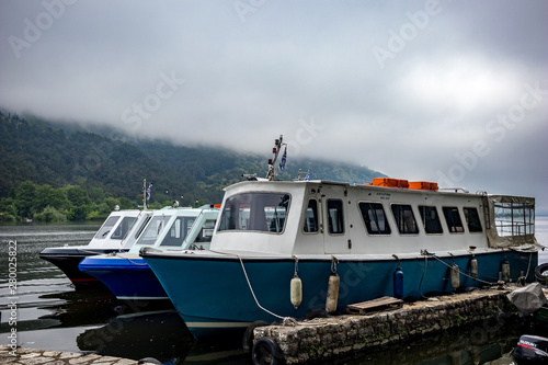 IOANNINA, GREECE - JUNE 6, 2019 - Three small old tourist cruise white and blue ferryboats moore on lake Pamvotida near the beautiful small Greek town. Early morning spring view with unusual fog