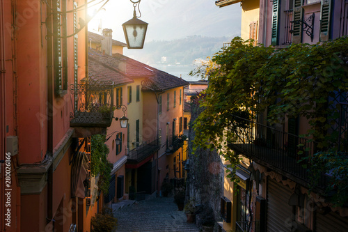 Narrow street with beautiful colourful houses with lantern and balcony in scenic Bellagio, Italy, region of Lombardy. The stairs down the Lake Como shore, mountains on the background. 