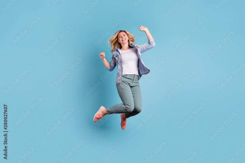 Full size photo of cute pretty woman jumping raising fists wearing pants trousers isolated over blue background