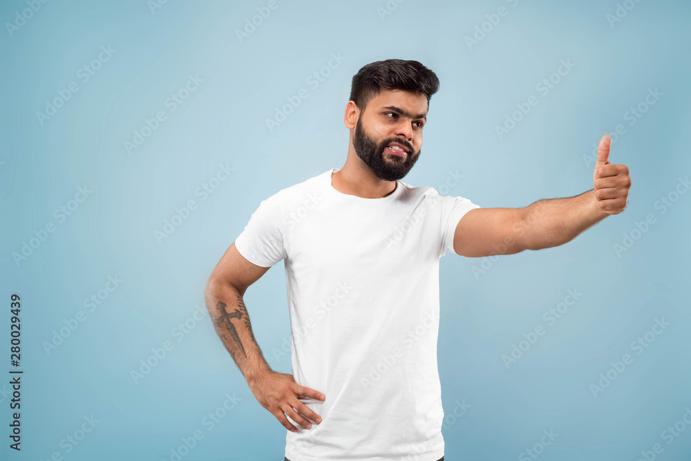 Half-length close up portrait of young hindoo man in white shirt on blue background. Human emotions, facial expression, ad concept. Negative space. Showing the sign of OK, nice, great. Smiling. Half-length close up portrait of young hindoo man in white shirt on blue background. Human emotions, facial expression, ad concept. Negative space. Showing the sign of OK, nice, great. Smiling.