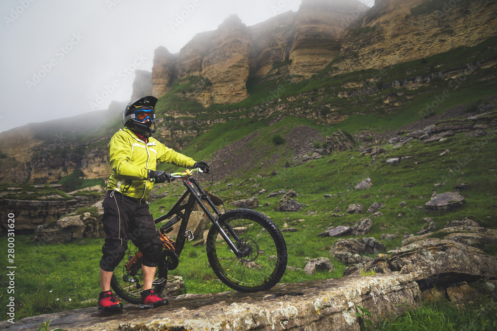 Side view of a man on a mountain bike standing on a rocky terrain and looking at a rock. The concept of a mountain bike and mtb downhill Side view of a man on a mountain bike standing on a rocky terrain and looking at a rock. The concept of a mountain bike and mtb downhill