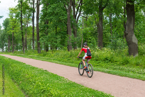 sportswoman riding a bike on a path in the forest among the tall green trees in the summer, Cycling