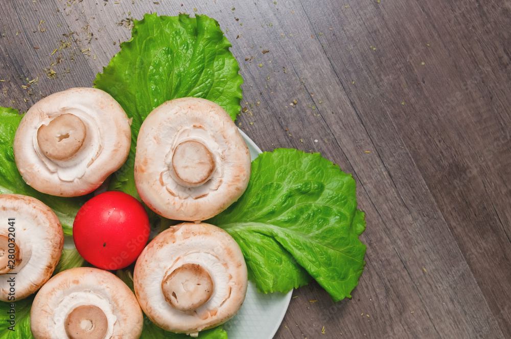Closeup of white mushrooms with green salad leaves with tomato on a dark wooden table. Vegetarian healthy food Closeup of white mushrooms with green salad leaves with tomato on a dark wooden table. Vegetarian healthy food