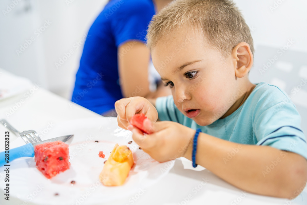 Little boy eating watermelon by the table at home Little boy eating watermelon by the table at home