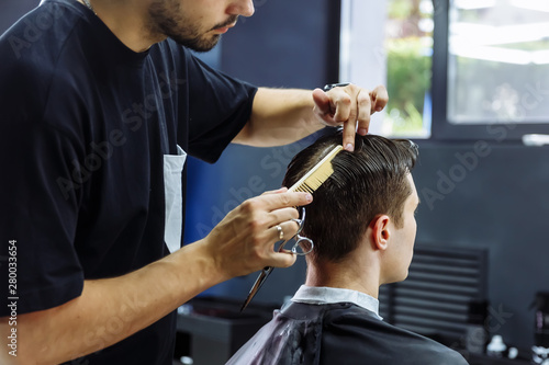 Barber cuts the hair of the client with scissors. Close up. Attractive male is getting a modern haircut in barber shop.