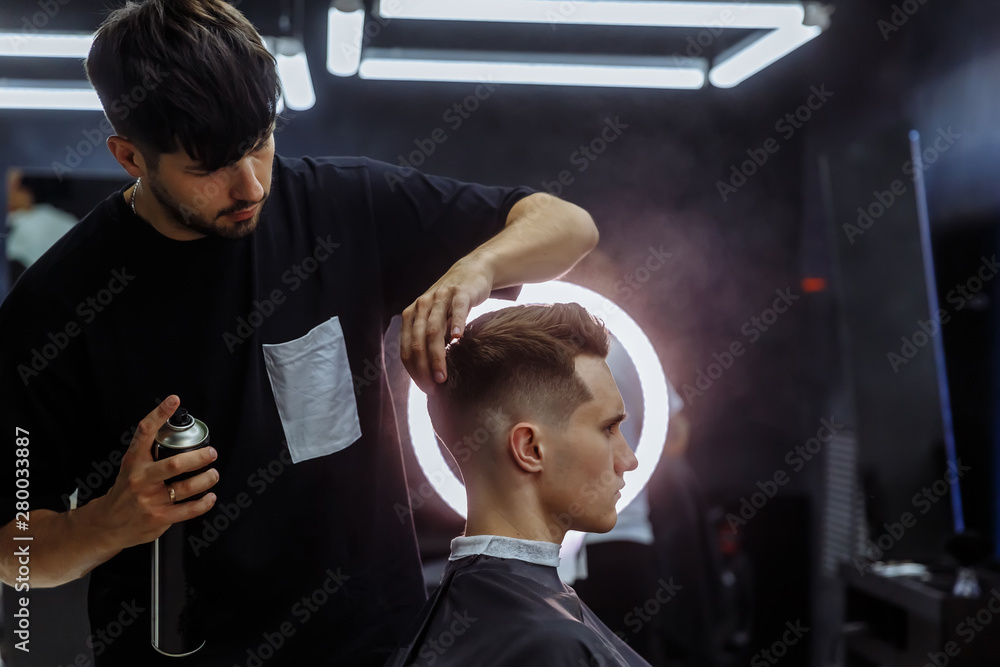 Barber makes hair styling with hair spray after haircut at the barber shop.  Young handsome Caucasian man getting a haircut in a modern hairsalon.  Stock-Foto | Adobe Stock
