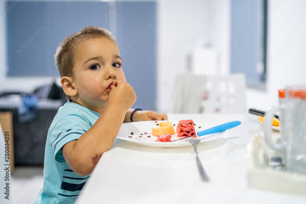 Little boy eating watermelon by the table at home Little boy eating watermelon by the table at home