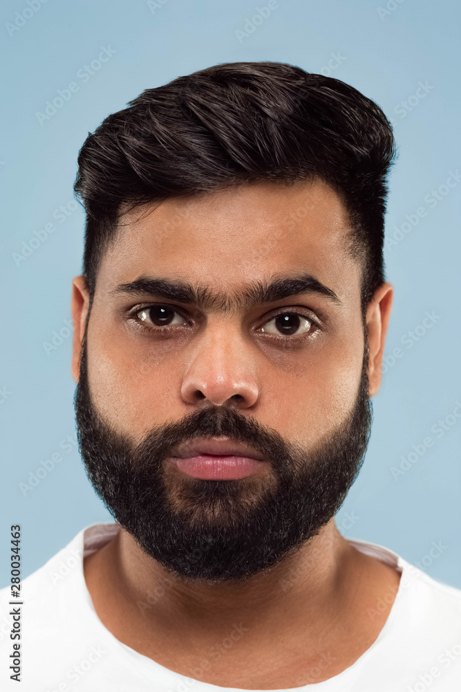 Close up portrait of young hindoo man with beard in white shirt isolated on blue background. Human emotions, facial expression, ad concept. Negative space. Standing and looking calm. Close up portrait of young hindoo man with beard in white shirt isolated on blue background. Human emotions, facial expression, ad concept. Negative space. Standing and looking calm.