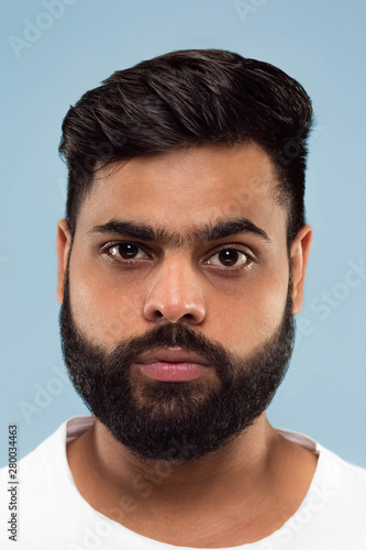 Close up portrait of young hindoo man with beard in white shirt isolated on blue background. Human emotions, facial expression, ad concept. Negative space. Standing and looking calm.