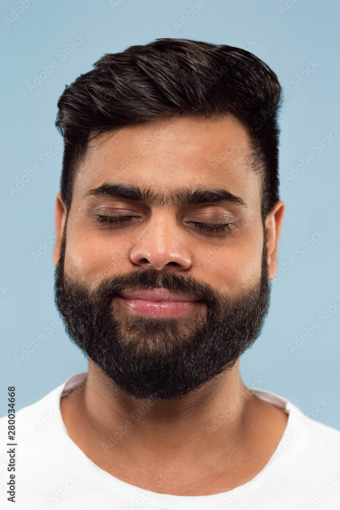 Close up portrait of young hindoo man with beard in white shirt isolated on blue background. Human emotions, facial expression, ad concept. Negative space. Dreaming with eyes closed. Close up portrait of young hindoo man with beard in white shirt isolated on blue background. Human emotions, facial expression, ad concept. Negative space. Dreaming with eyes closed.