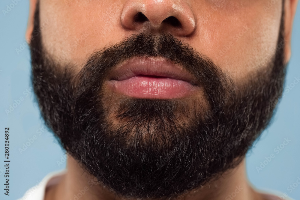 Obraz premium Close up portrait of young hindoo man's face with beard and lips on blue background. Looking calm. Human emotions, facial expression, advertising concept. Negative space.