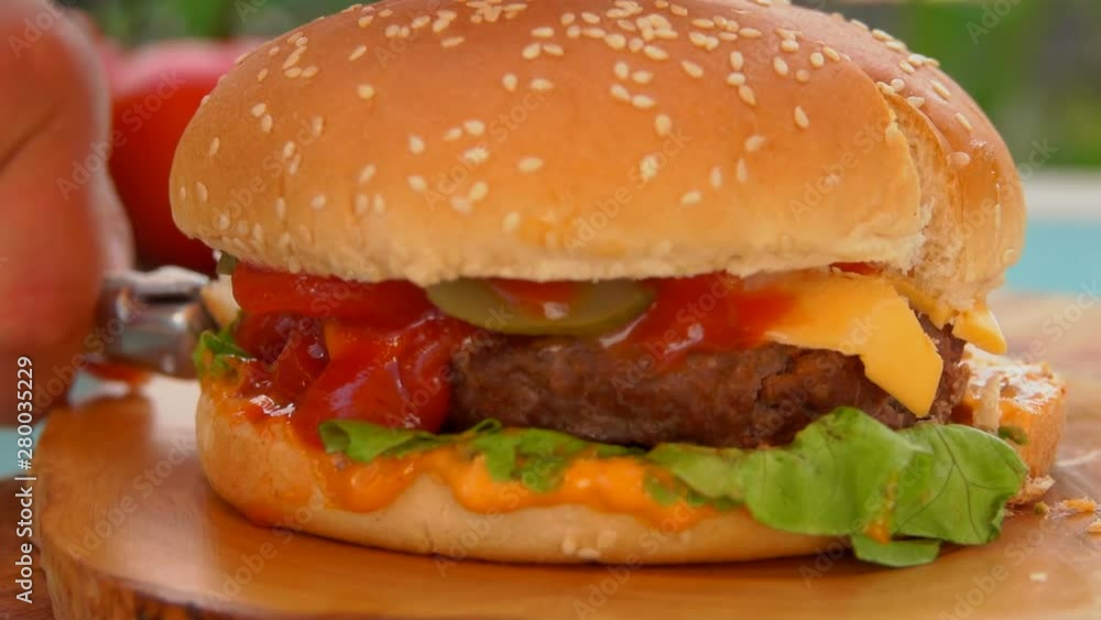 Knife cuts into half a delicious hamburger with cheese and tomatoes Knife cuts into half a delicious hamburger with cheese and tomatoes