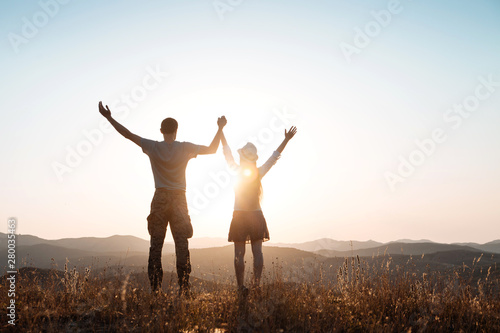 The guy and girl stands among the mountains and greet the sun
