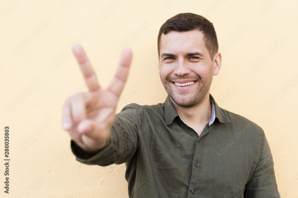 Stubble young man showing peace gesture on beige backdrop Stubble young man showing peace gesture on beige backdrop