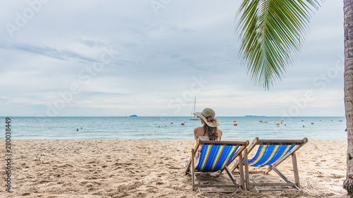 Summer beach vacation holidays trip concept, Happy young Asian woman with hat relaxing on beach chair and raised hands up.