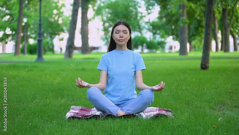 Attractive young lady meditating in park sitting lotus pose, relaxing outdoors Attractive young lady meditating in park sitting lotus pose, relaxing outdoors