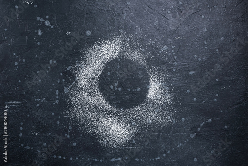 Circle of powdered sugar on a dark stone surface.Top view.