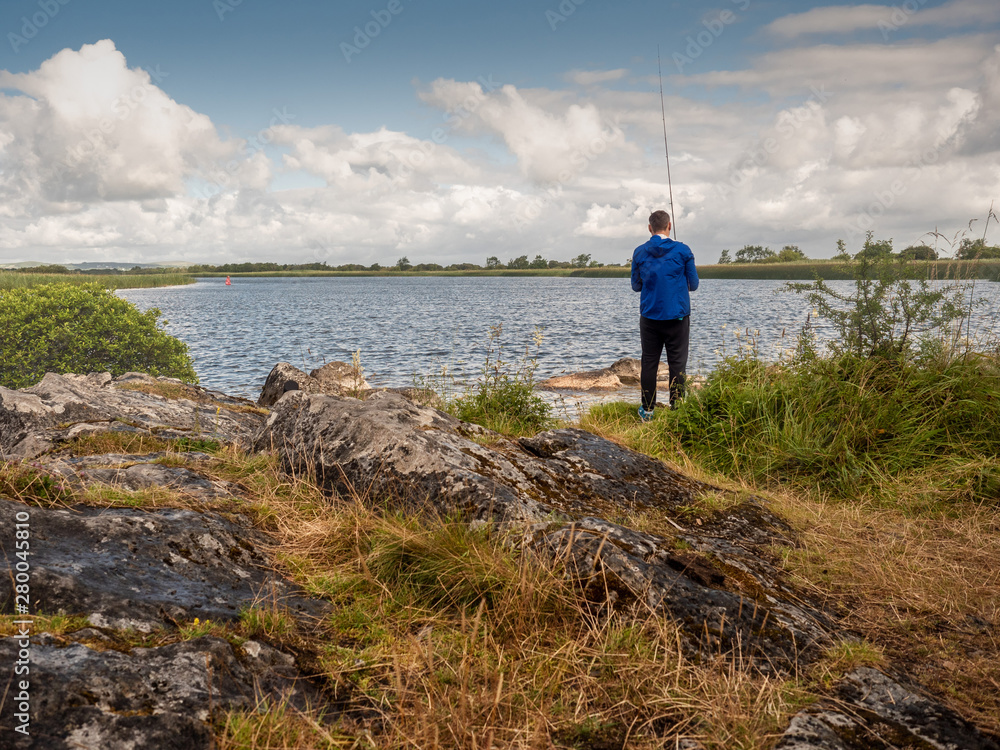 Man in blue jacket fishing on a river with spinning. Warm sunny day, Cloudy sky. Man in blue jacket fishing on a river with spinning. Warm sunny day, Cloudy sky.