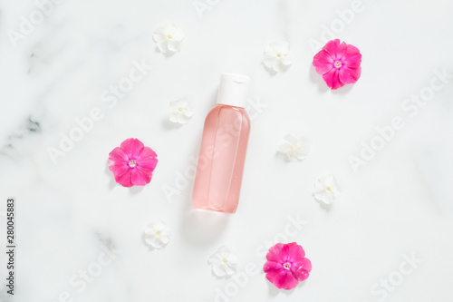 Cosmetic package containers with pink liquid lotion and flower petals on marble background. Minimal flat lay style composition, top view, overhead. Bio organic product, beauty and spa concept.