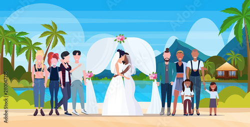 couple newly weds lesbians in white dress standing behind arch same gender married homosexual family wedding celebrating concept tropical island seascape landscape background full length horizontal