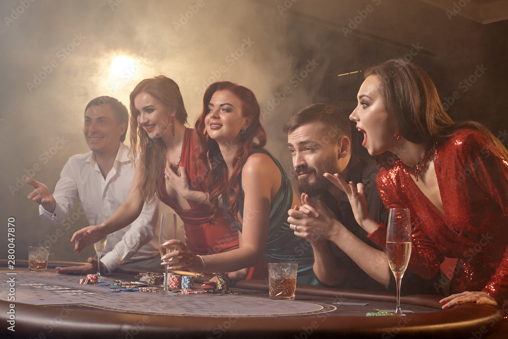 Group of a young wealthy friends are playing poker at a casino. - obrazy, fototapety, plakaty 