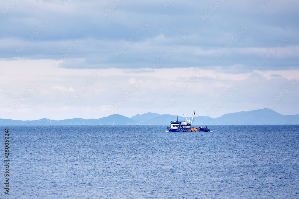 Blue trawler fishing boat sailing over the calm sea in a cloudy winter day in Gumusluk, Bodrum, Turkey. Blue trawler fishing boat sailing over the calm sea in a cloudy winter day in Gumusluk, Bodrum, Turkey.