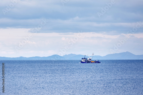 Blue trawler fishing boat sailing over the calm sea in a cloudy winter day in Gumusluk, Bodrum, Turkey.