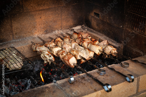 Close-up on the process of cooking barbecue of pork or beef meat mounted on skewers in a grill with a crispy burnt crust over gray burnt coals on an open fire. Picnic and food in nature and outdoor.
