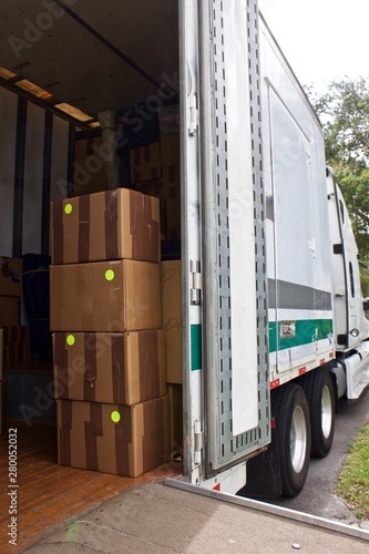  Moving van interior with packed boxes by open door with bright identity labels or writing on each to identify what room they go to. movers use dollies and hand trucks on loading ramp for furniture an