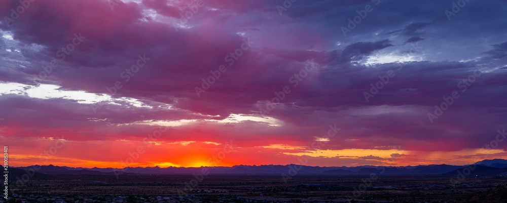 Panorama of colorful clouds at sunset over an urban environment with mountains in the distance