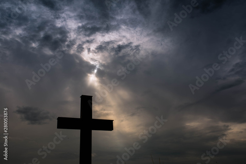 Silhouette of a simple catholic cross, dramatic stormclouds after heavy rain, copy space.