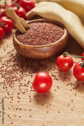 selective focus of red quinoa in wooden bowl with spatula near beige napkin and scattered tomatoes