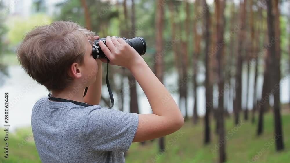 Closeup side view of cute curious kid exploring nature using old vintage binoculars. Boy standing in green old pine wood on summer day. Real time full hd video footage. Closeup side view of cute curious kid exploring nature using old vintage binoculars. Boy standing in green old pine wood on summer day. Real time full hd video footage.